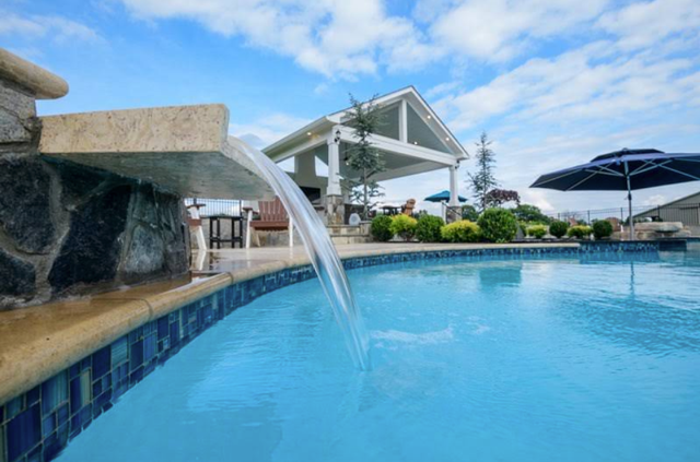 Resort pool with a stone waterfall and blue umbrellas under a bright sky