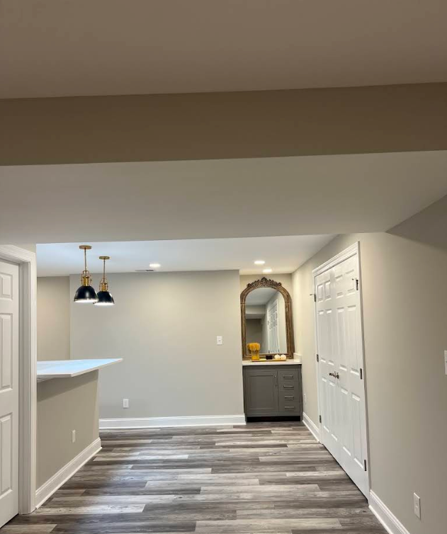 Empty modern kitchen and dining area with gray walls, white trim, pendant lights, and wood-look flooring