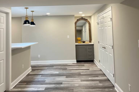 Empty modern room with gray walls, wood-look flooring, pendant lights, and a mirrored vanity by white closet doors