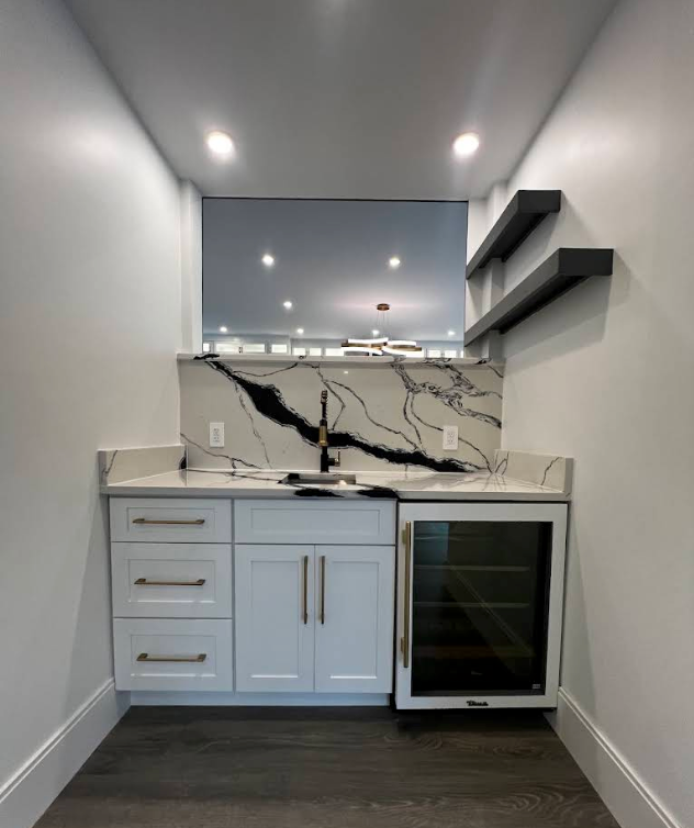 Narrow wet bar with white cabinets, marble backsplash, mirror, and wall shelves under recessed lights