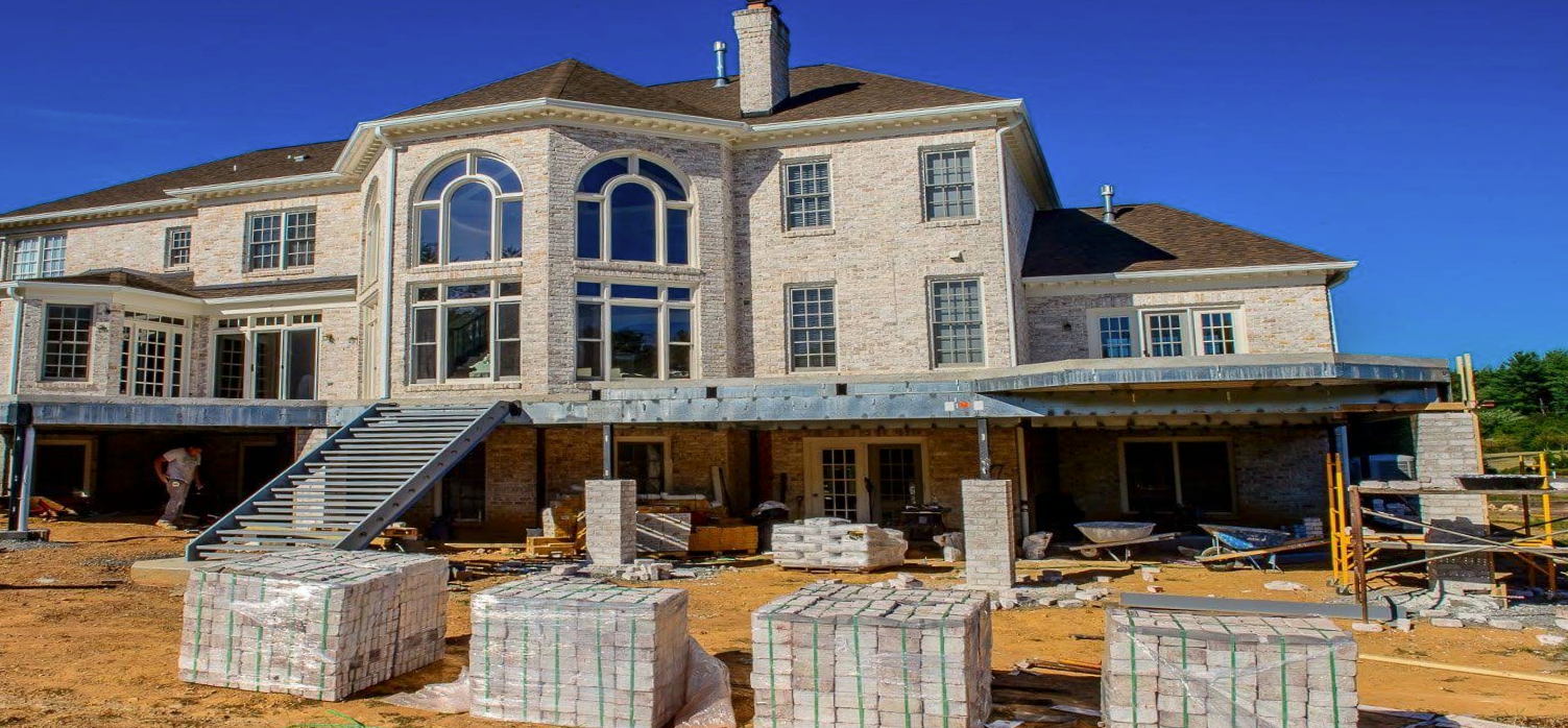 Large stone house under construction with stacked building materials in the front yard