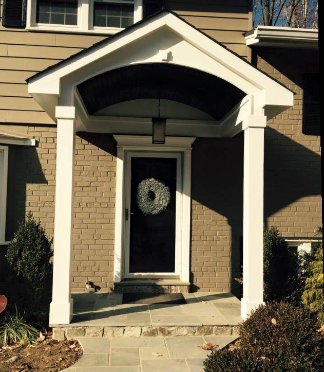 Front entrance of a brick house with white trim, arched porch roof, and a black door with a wreath