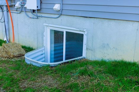 Basement window well beside a house, with white-framed window and green grass outside