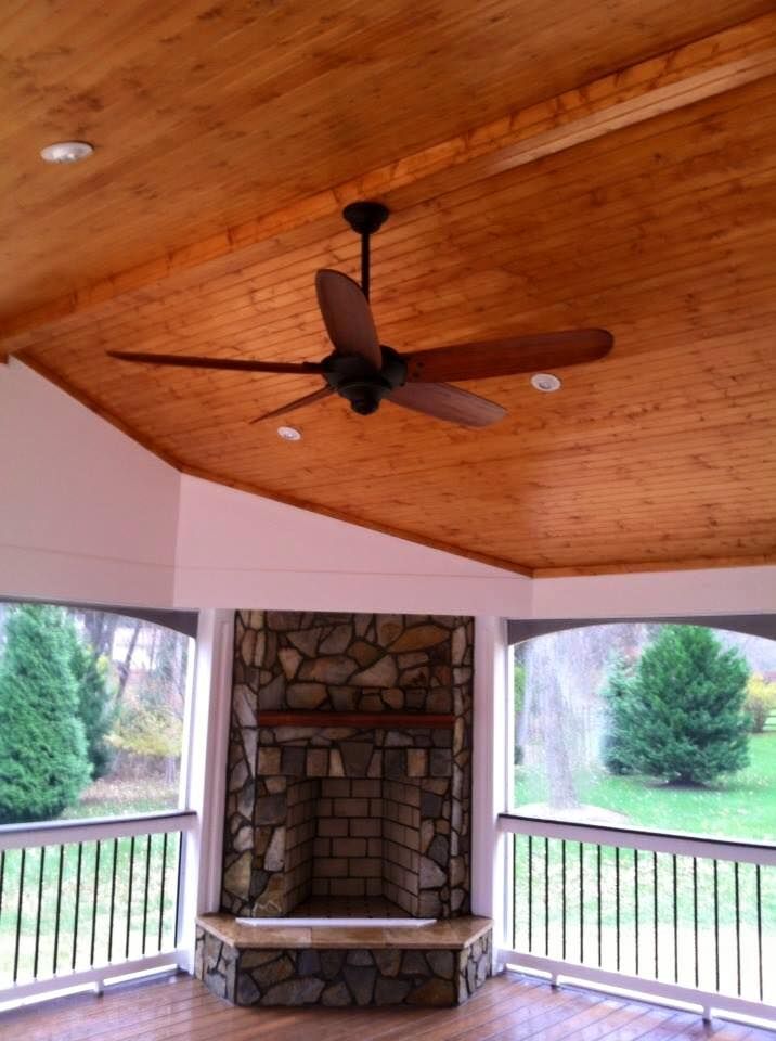 Covered porch with wood ceiling fan, stone fireplace, and open view of a grassy yard