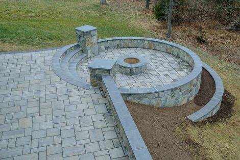 Stone outdoor fireplace and low wall in a sunny landscaped park with trees and grass