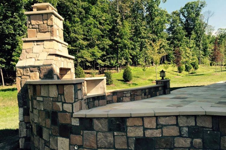 Stone outdoor fireplace with bench seating beside a grassy park and trees