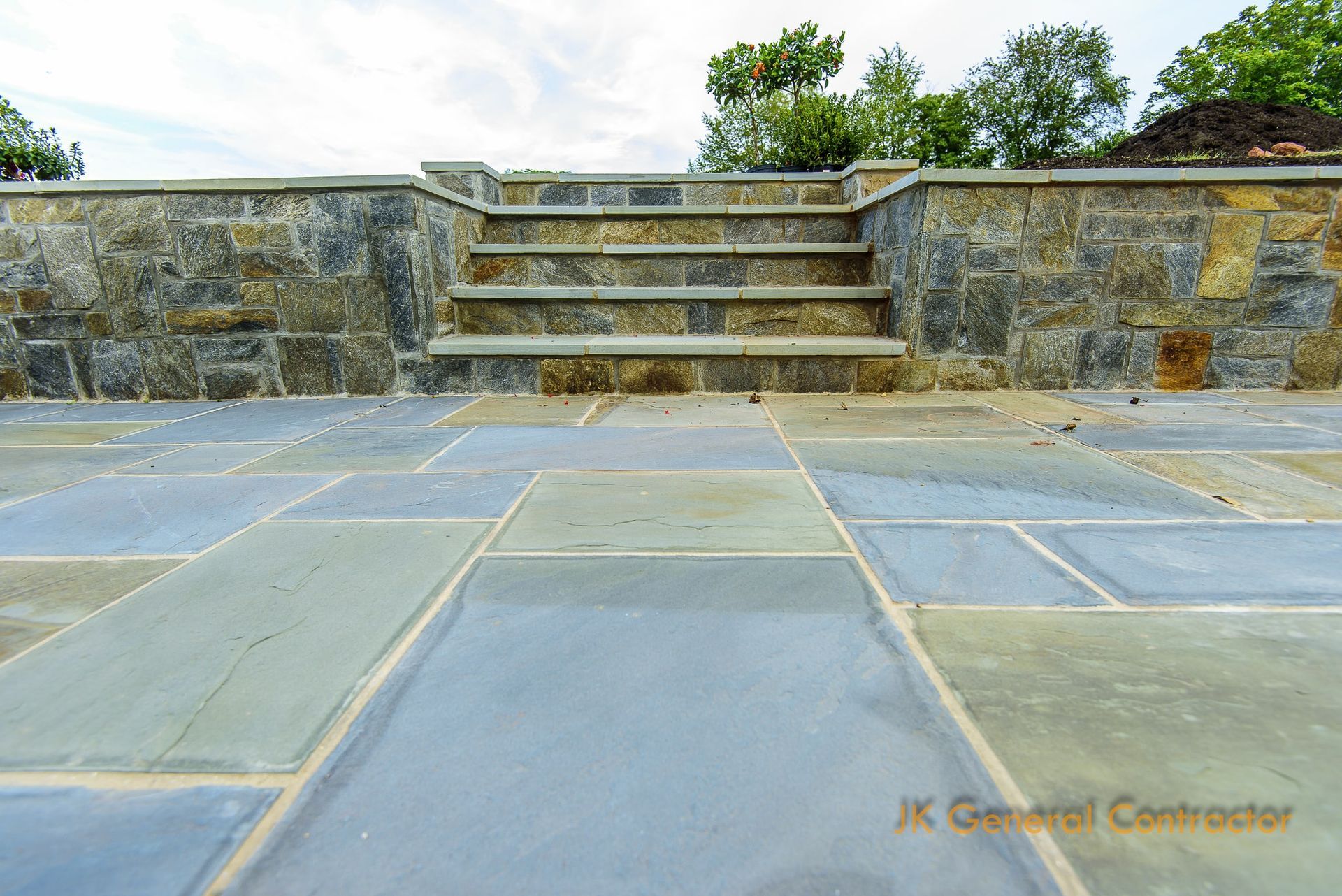 Stone patio and steps leading to a raised terrace with stone walls and greenery