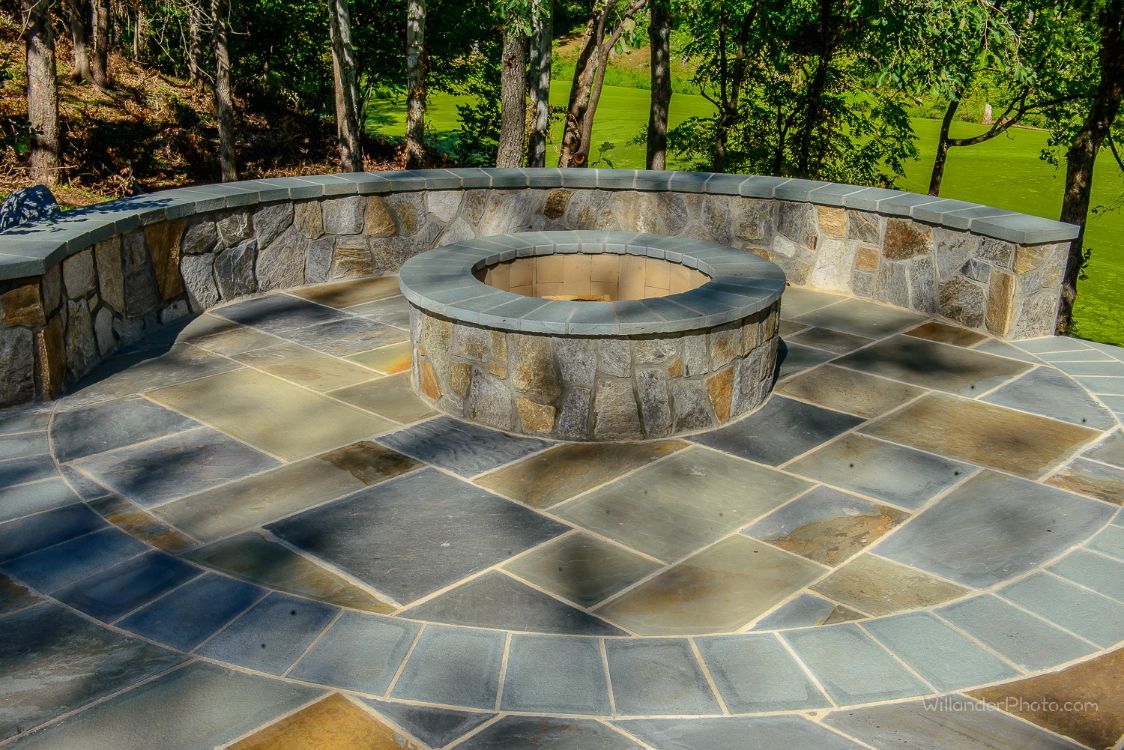 Stone memorial bench and circular fire pit on a flagstone patio in a wooded park