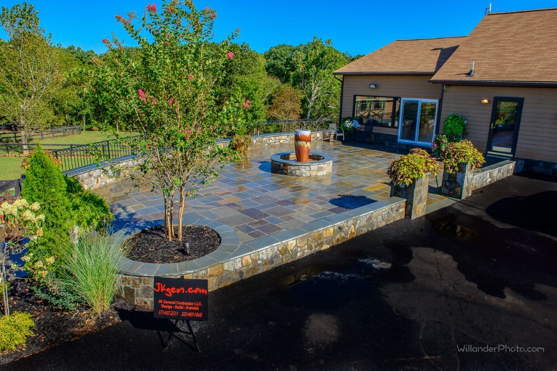 Backyard patio with pavers, potted trees, and a small fountain beside a house