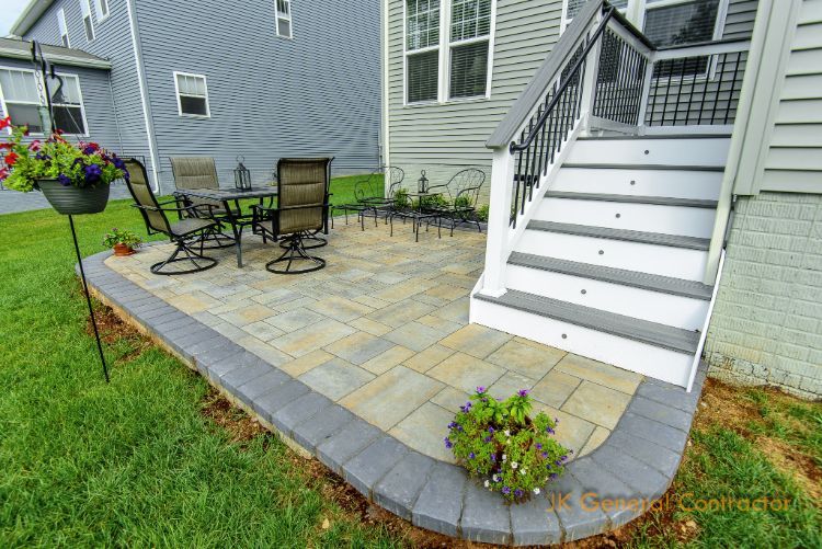 Back patio with stone pavers, outdoor table and chairs, flower pots, and white stairs beside a house