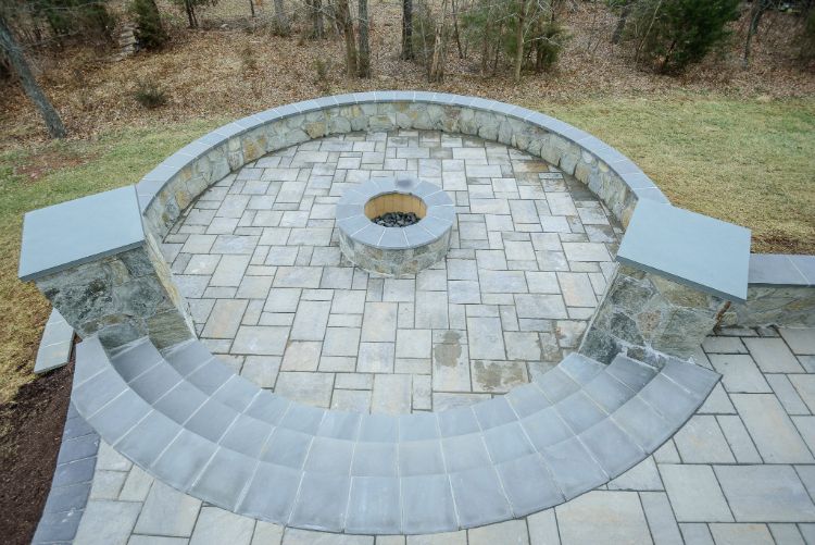 Stone outdoor amphitheater with curved seating and a central fire pit surrounded by pavers.