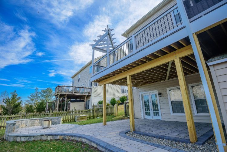 Backyard deck and patio under a house, with white railings, wooden posts, and a stone walkway