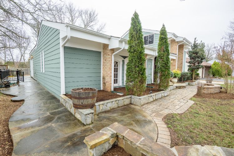 Suburban house with light blue siding, stone porch, ivy-covered columns, and a curved walkway