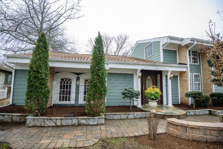Suburban stone house with white trim, green siding, and a landscaped front entryway