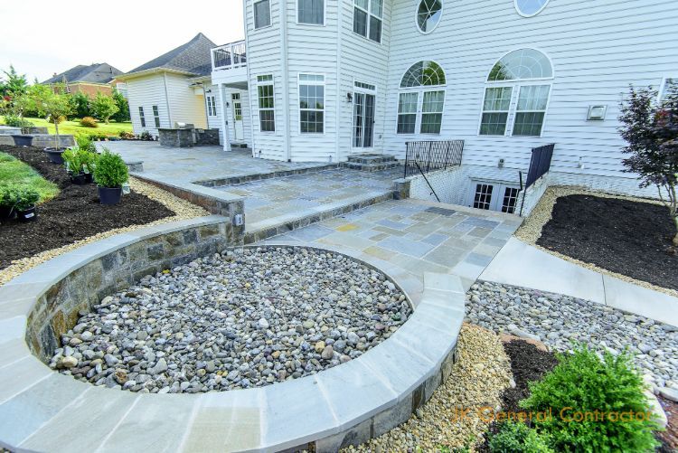White house patio with curved stone planter, gravel landscaping, and outdoor seating