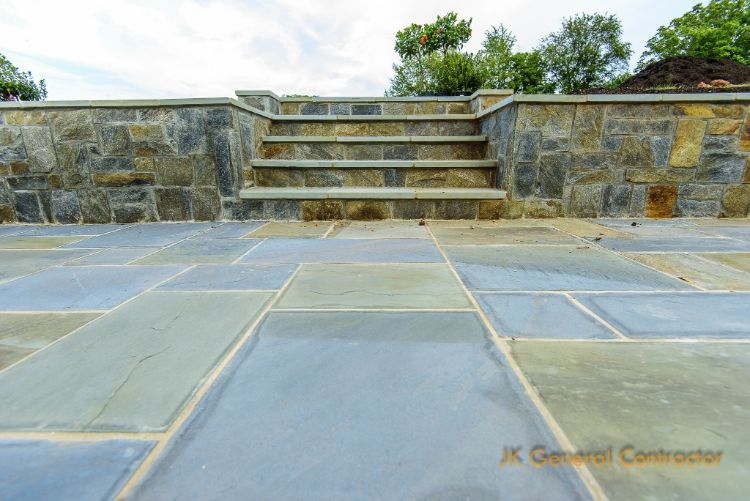Stone patio with steps leading to a raised wall and greenery in the background