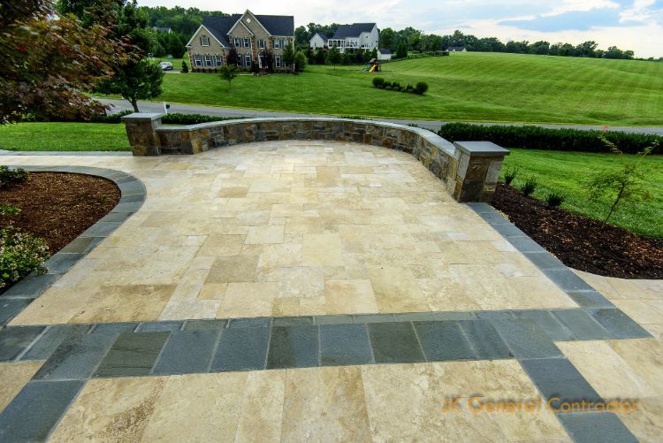 Curved stone patio with low walls overlooking a green lawn and distant houses under cloudy sky