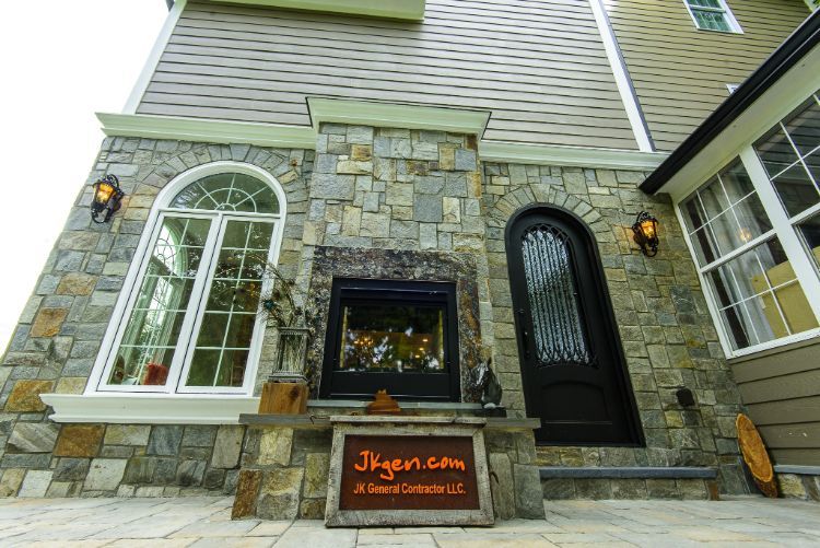 Stone building entrance with arched windows, black door, and a lit sign by the walkway.
