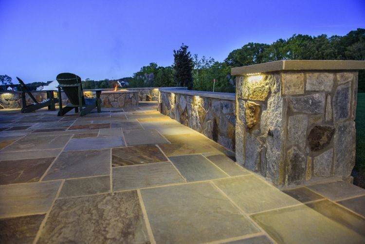 Stone patio with outdoor seating, lit stone walls, and trees at dusk