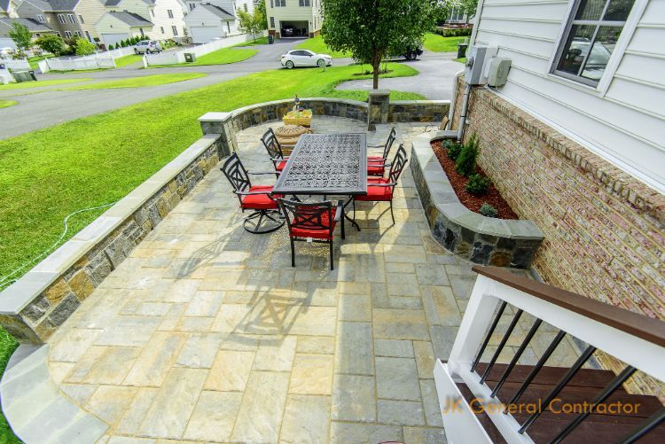 Patio with stone pavers, red chairs, black table, and built-in stone planter beside a house