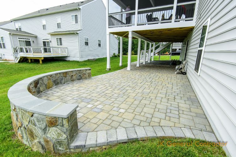 Curved stone patio beside white house with raised deck and grassy yard