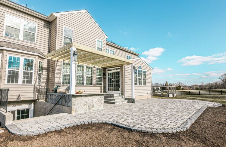 Spacious beige house with stone patio and covered back porch under a bright blue sky