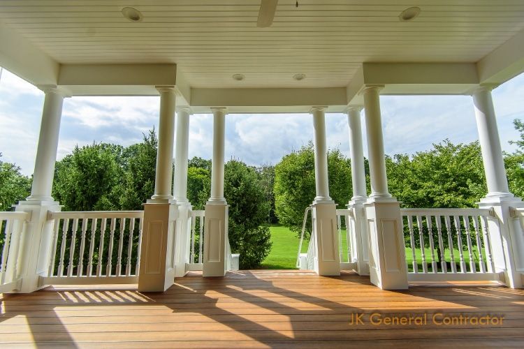 Covered wooden porch with white railings overlooking a sunny green yard