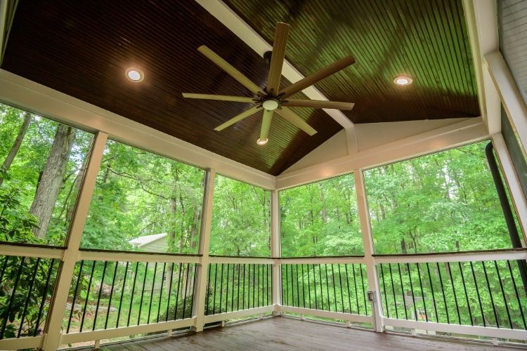 Covered porch with green forest views, wood railing, and a dark ceiling with a ceiling fan