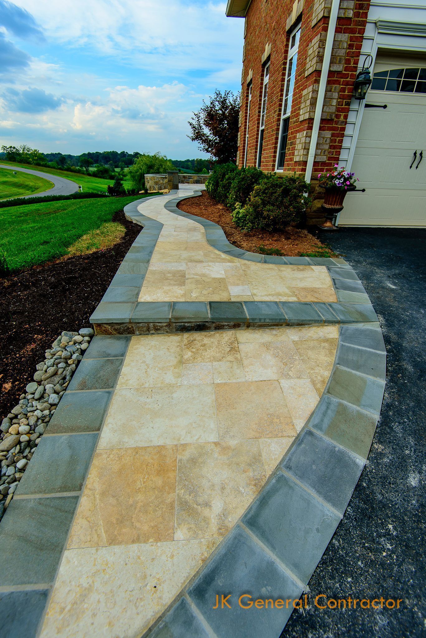 Stone patio steps and a stone retaining wall in a sunny outdoor yard with a house in the background
