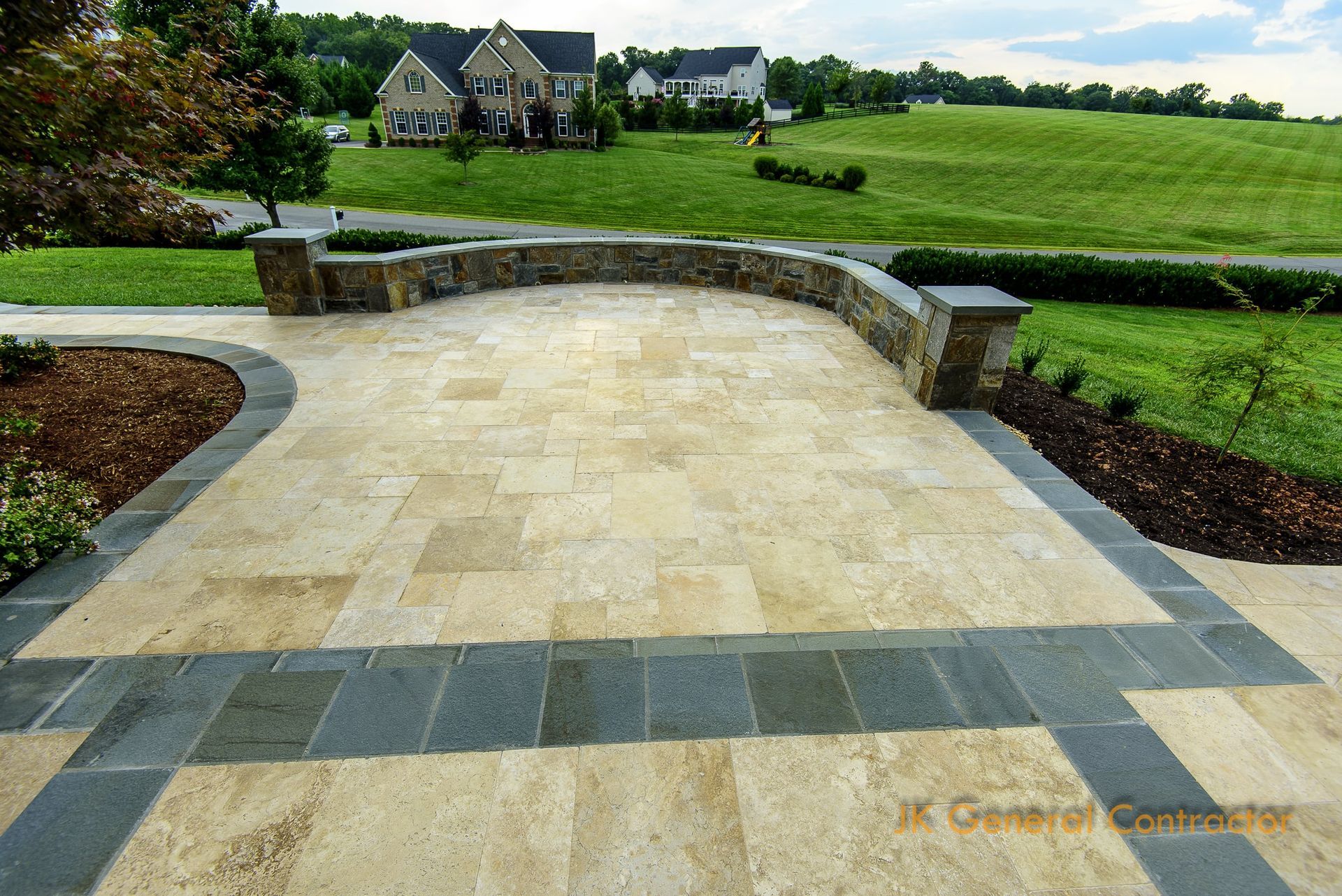 Stone patio with low curved wall overlooking a green lawn and distant houses in a rural landscape