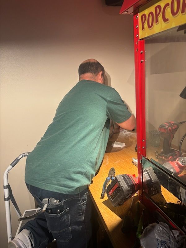 Man in a green shirt operating a popcorn machine at a concession stand