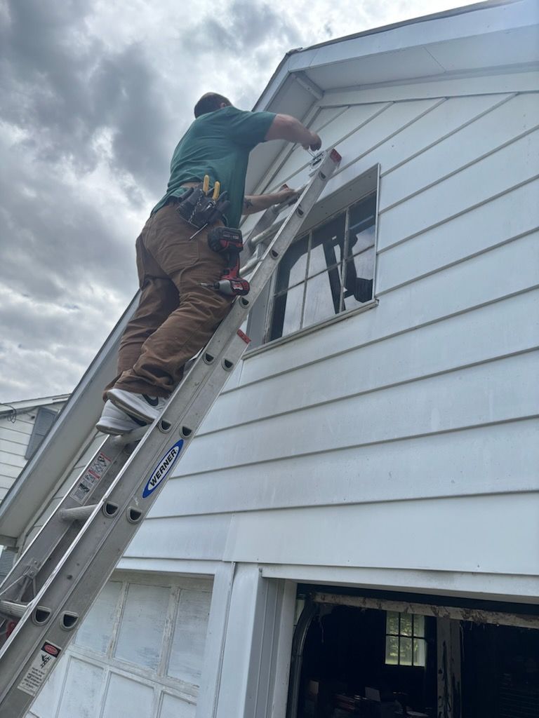Worker on ladder repairing a second-story window on a white house