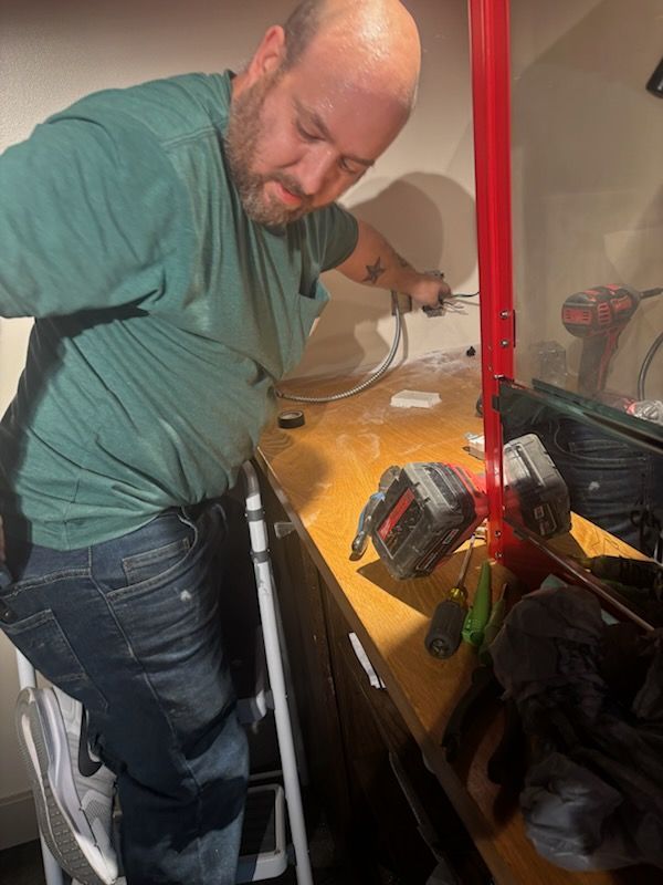Man leaning into a kitchen cabinet, reaching toward items on a wooden counter beside a red pole.