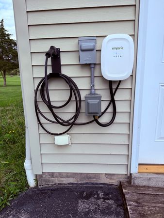 Exterior wall with utility boxes, coiled black cable, and a white device mounted beside a door