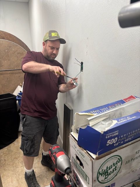 Man painting a wall beside stacked boxes, holding a brush and roller in a small room.