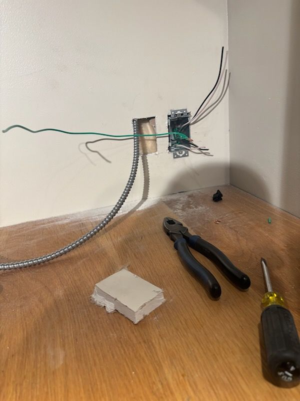 Electrical wires and tools on a wooden floor beside a wall outlet box installation