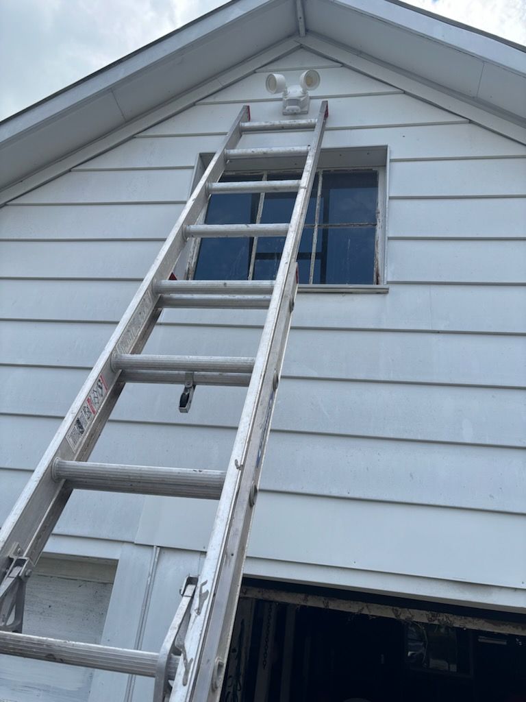 Ladder leaning against a white house under a peaked roof, reaching toward an upper window.
