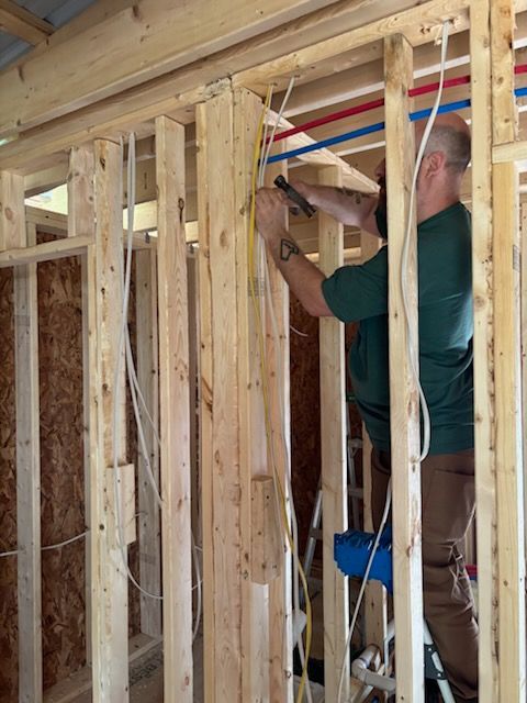 Worker installing wiring in a wooden wall frame during home construction