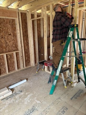 Worker standing on a green ladder framing an unfinished interior wall in a house under construction