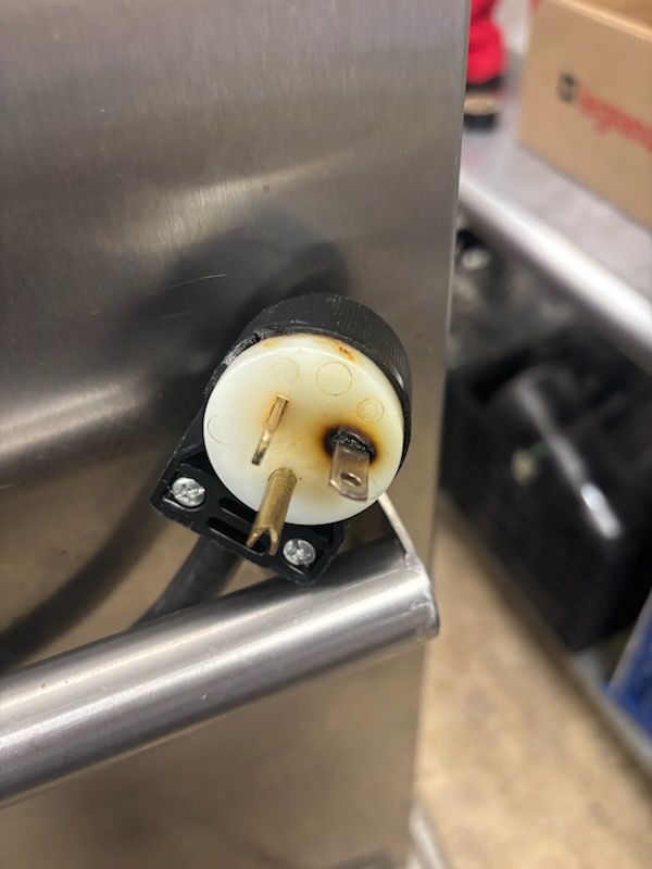 Close-up of a white plastic electrical connector mounted on a stainless steel surface.