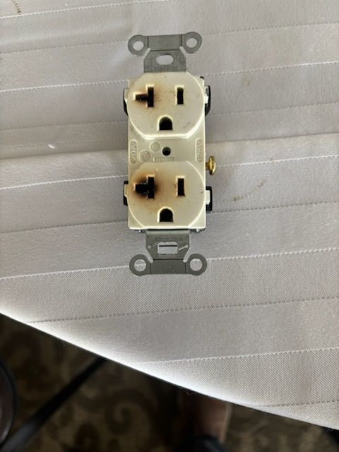 White electrical outlet on a quilted light-gray surface, viewed from above.