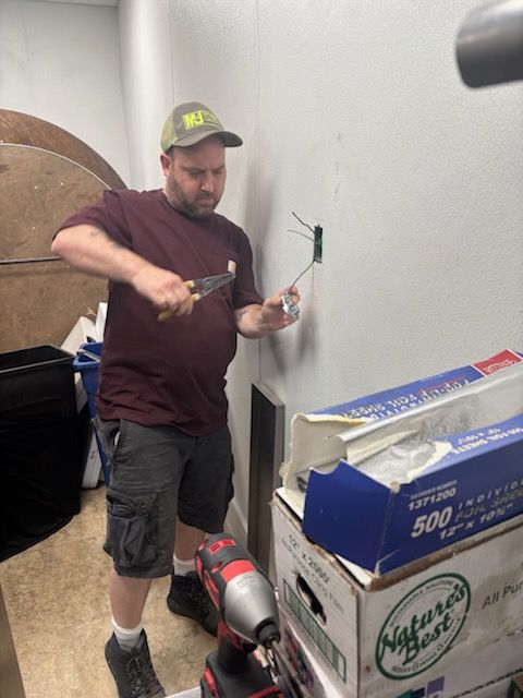 Man using a drill to work on a wall beside stacked boxes in a room