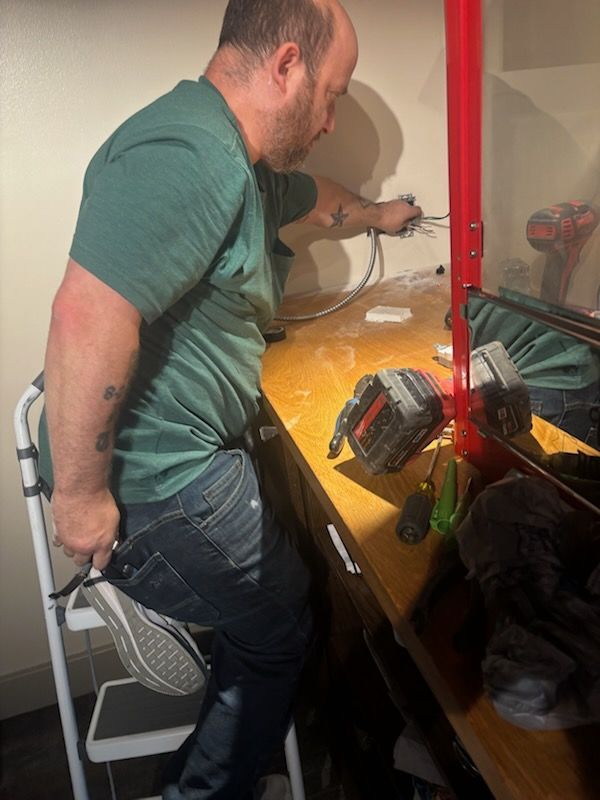 Man fixing wiring at a workbench with tools and a red lamp