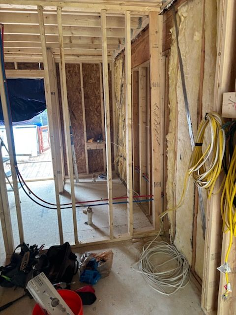 Unfinished room with exposed framing, hanging wires, and construction tools on the floor.