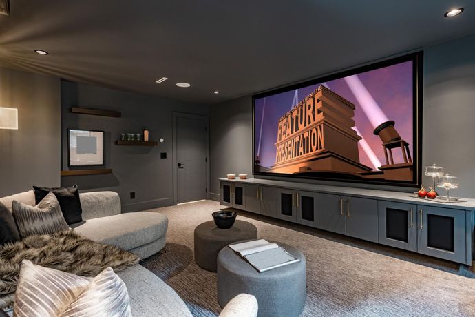 Modern home theater with plush gray seating and a large screen showing a movie studio logo