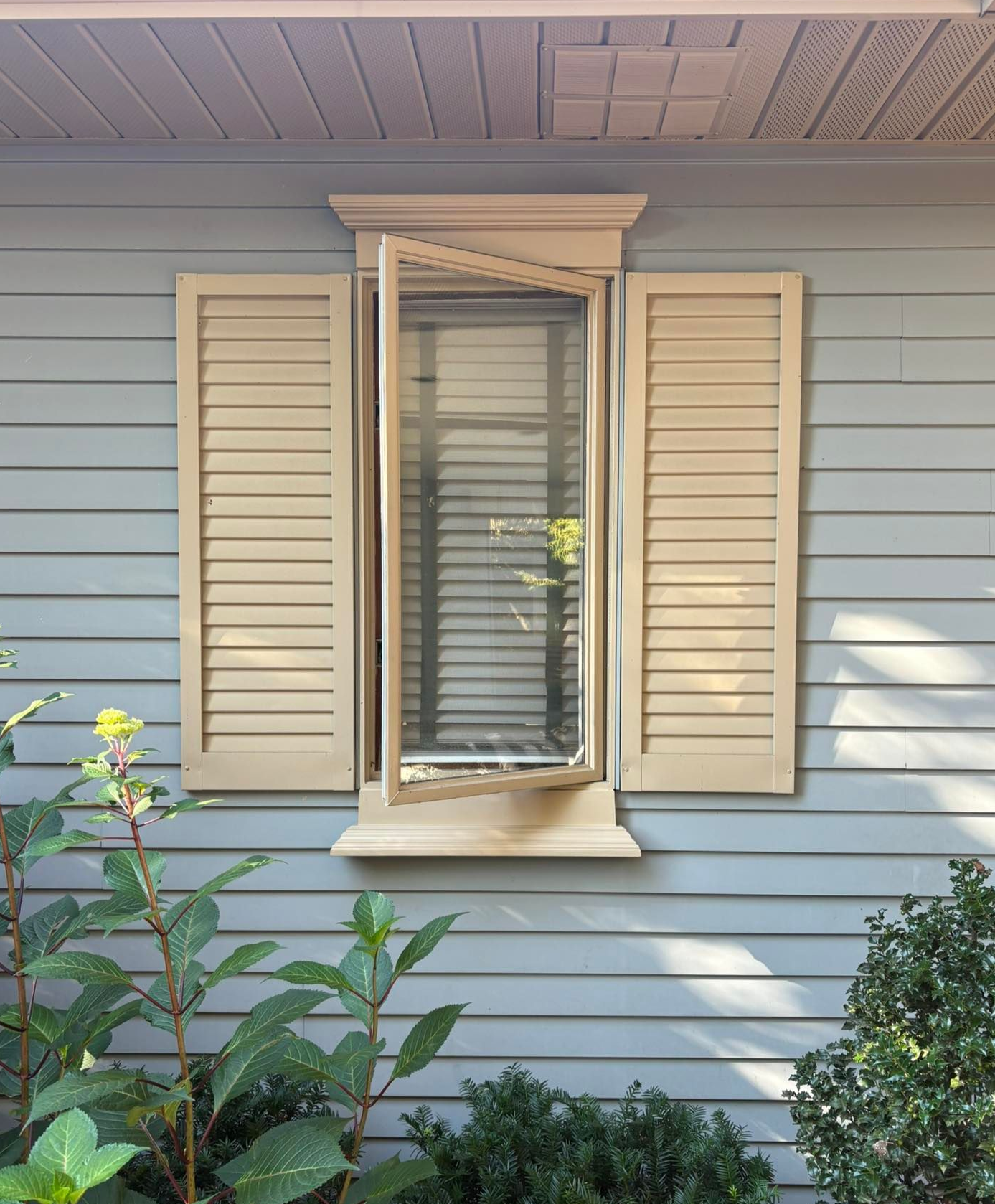 White double-hung windows with screens set into a wall with light-colored horizontal siding above a stone facade.