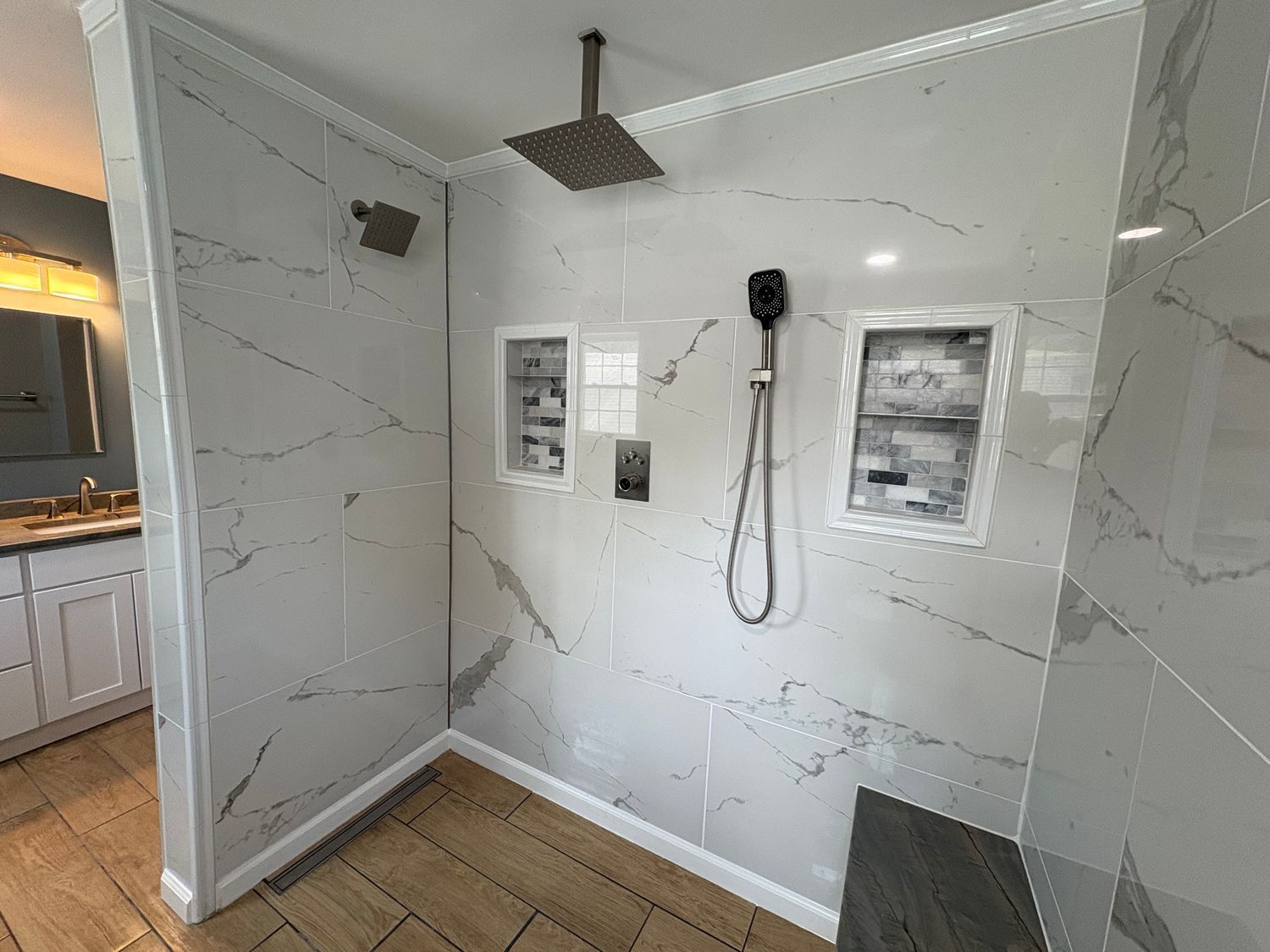 A tiled walk-in shower stall with white walls and a white floor, featuring a silver shower head and control handle.