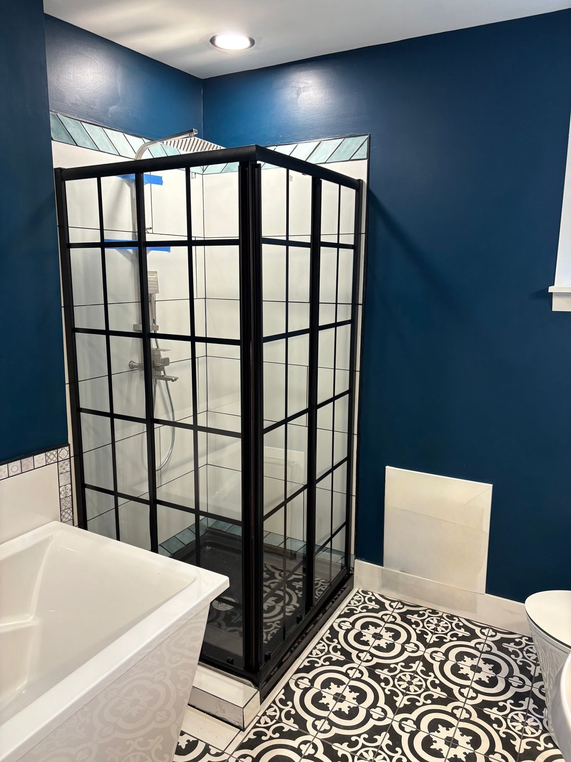 A bathroom with a black-framed grid shower, navy blue walls, and patterned black-and-white floor tiles.