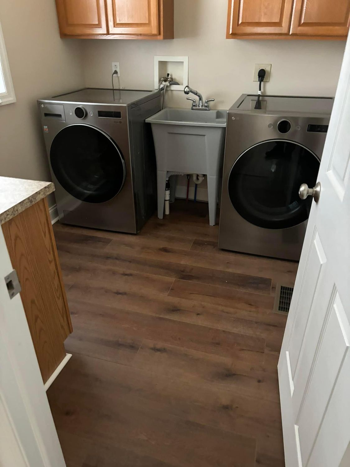A laundry room with two gray, front-load appliances and a central gray utility sink beneath wooden wall cabinets.