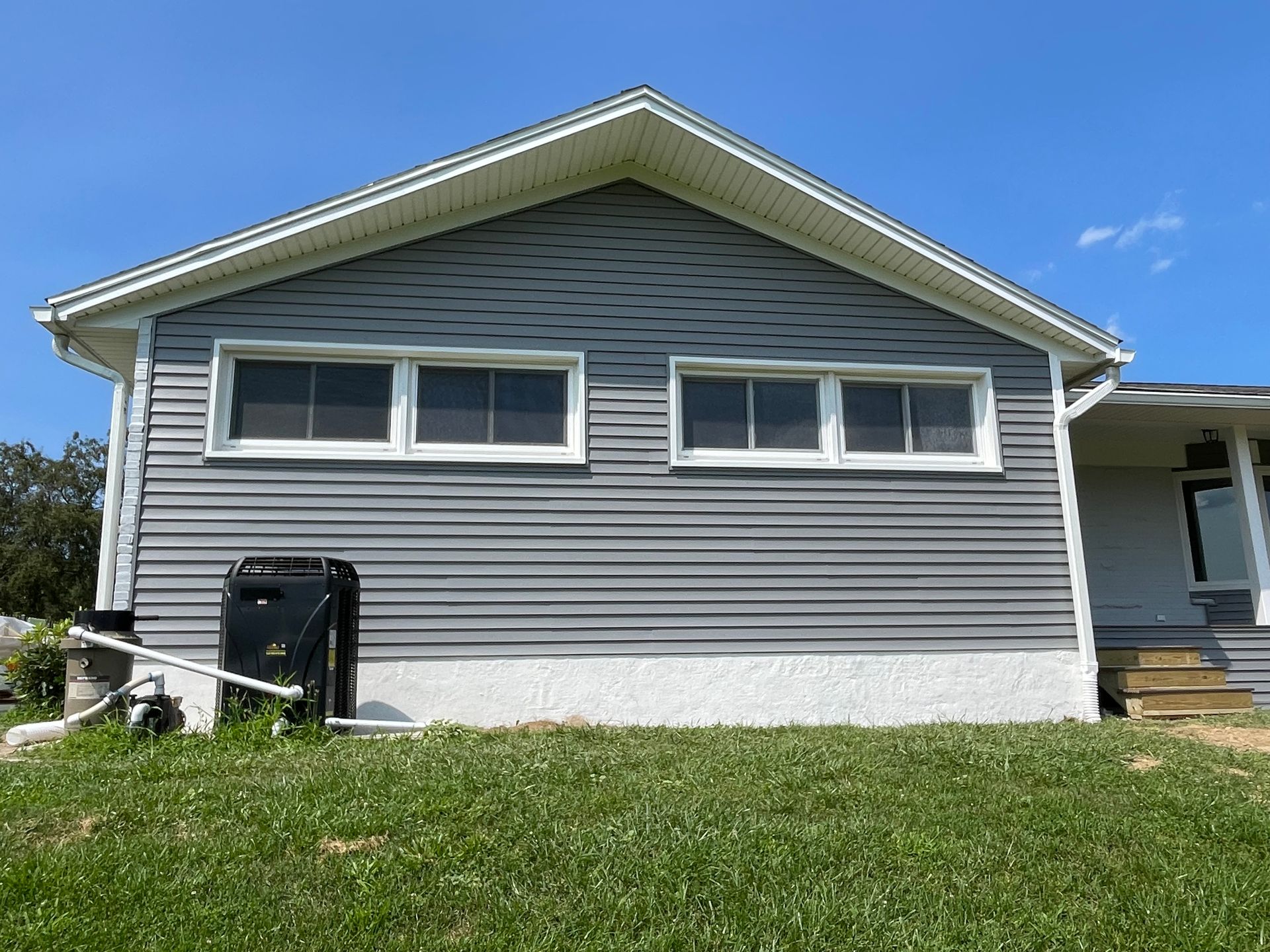 A gray, vinyl-sided house exterior with two sets of windows above a white foundation, set against a clear blue sky.